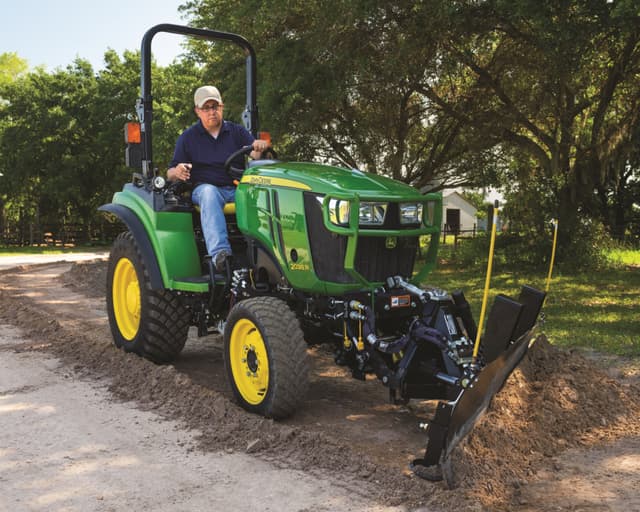 A man operates a compact tractor with a scraper attachment.