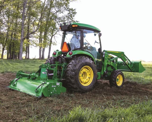 A John Deere tractor with attachments plows a field.