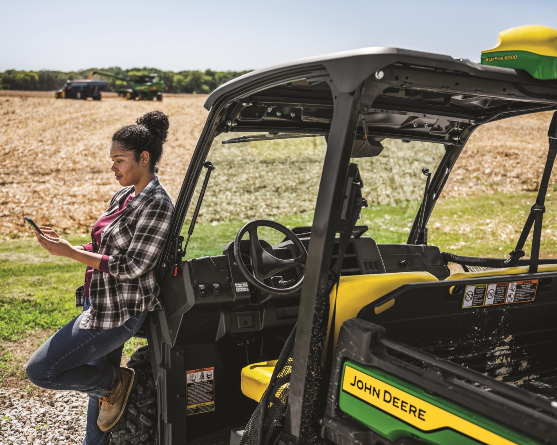 A Gator operator stands beside her Gator while surveying a field.