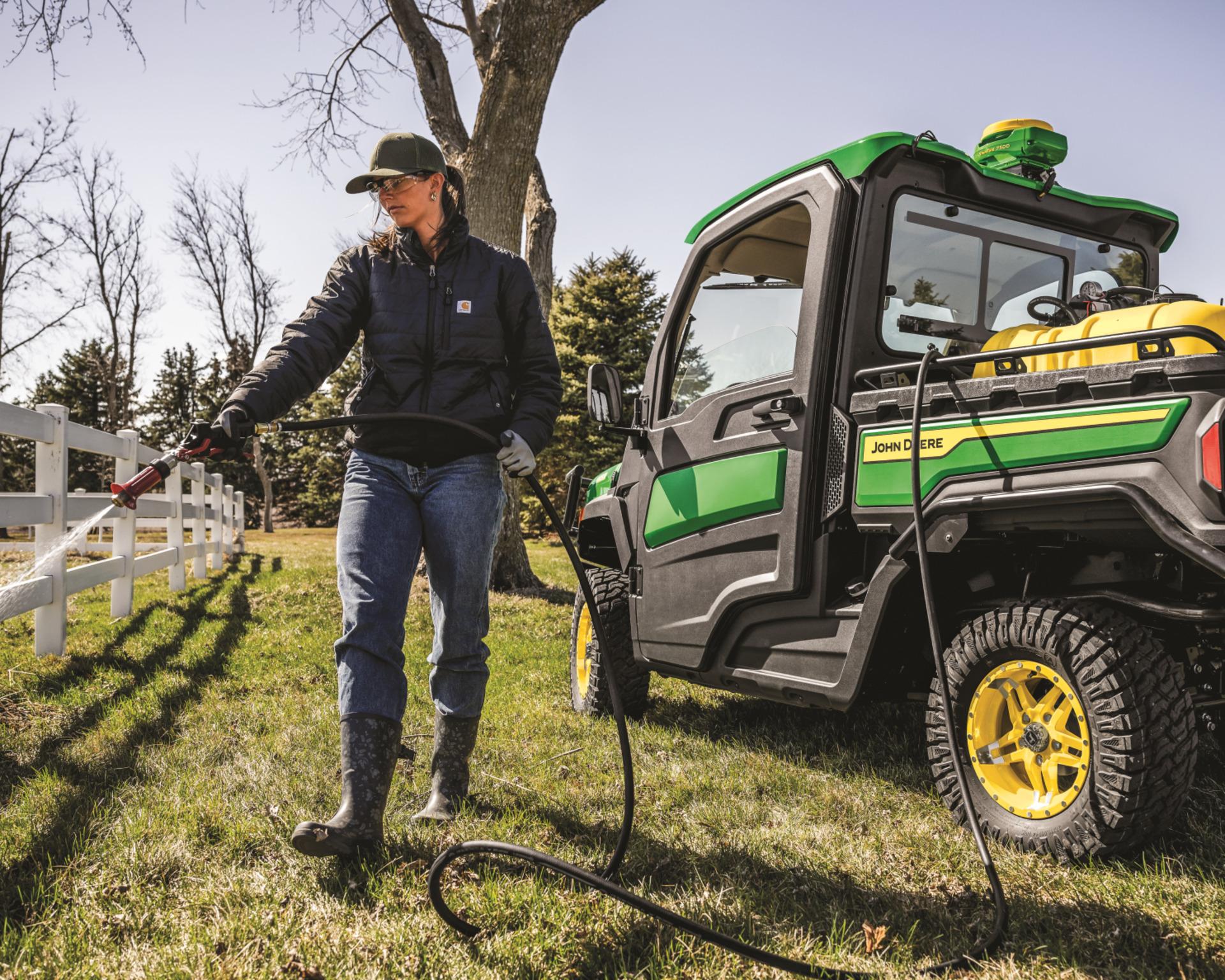 A woman sprays for weeds along a fence line using her Gator sprayer attachment.