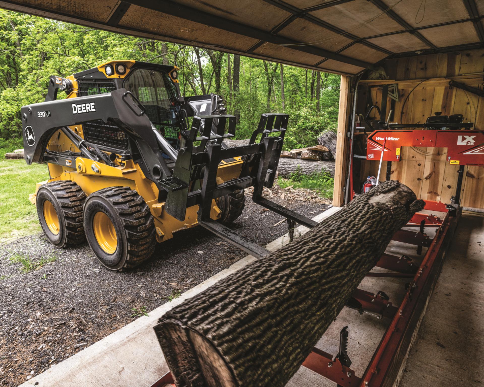 A John Deere 330 P Tier skid steer lifts a log.