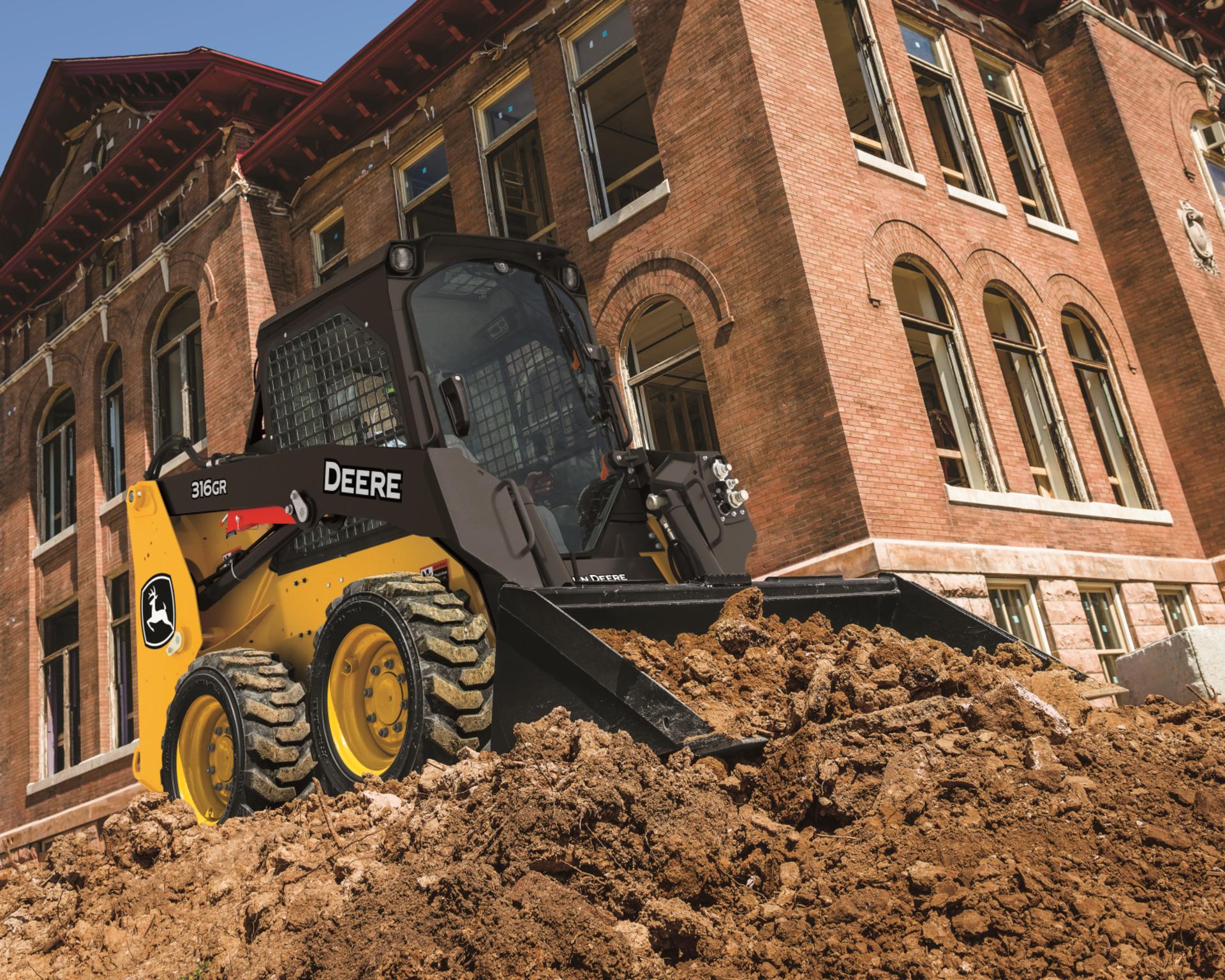 A John Deere 316GR moves dirt on a job site.