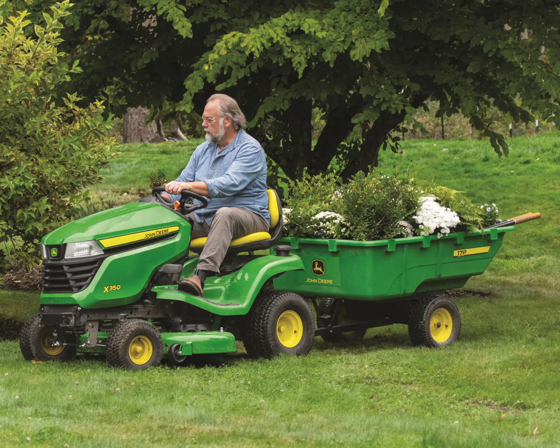 A John Deere X350 with a trailer is used by a homeowner to maintain their property.