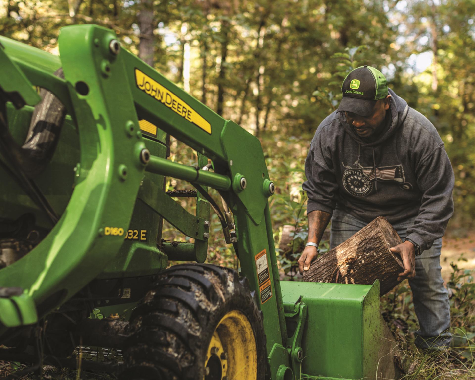 A man loads wood into the front-end loader of a John Deere 3032E.