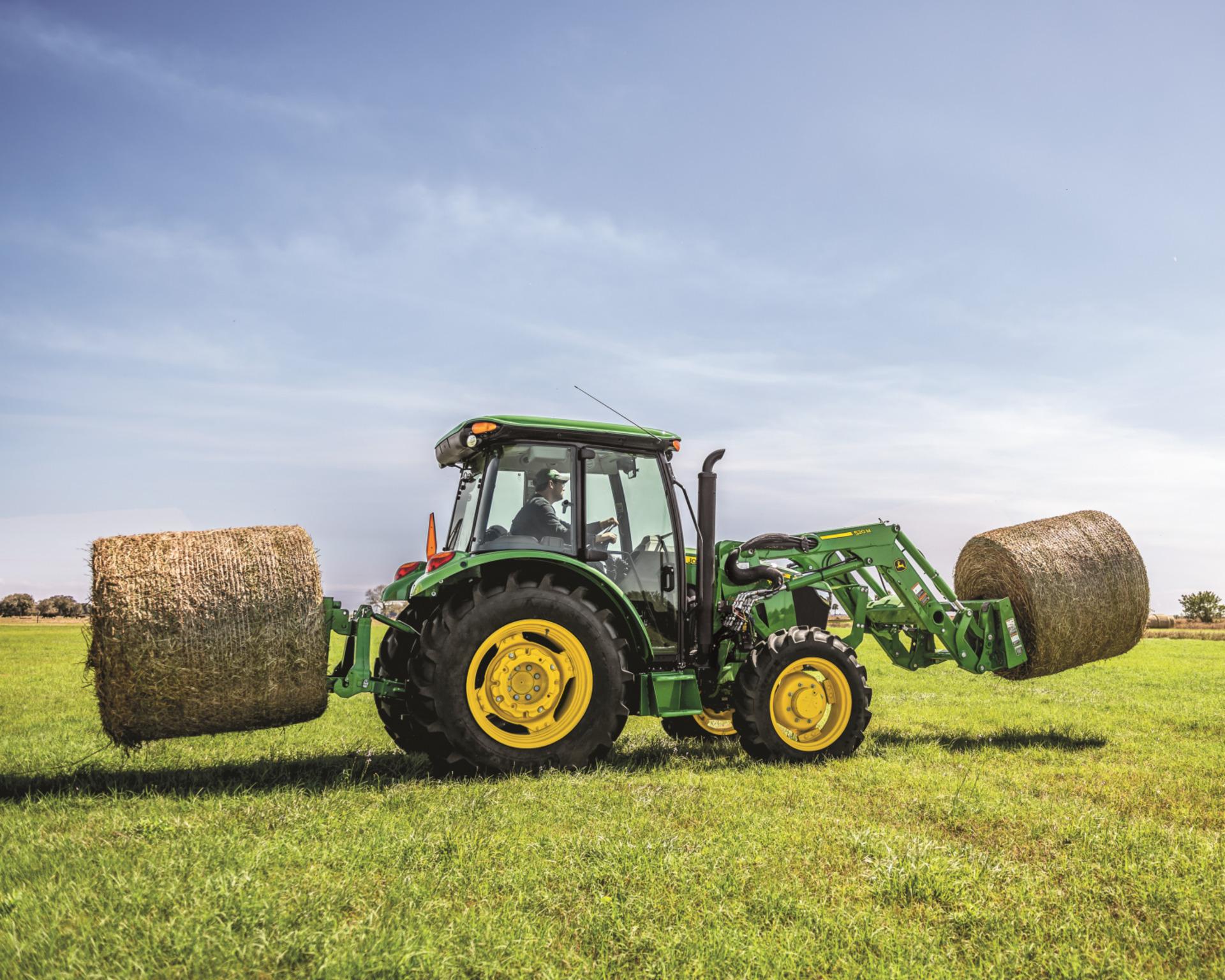 A John Deere 5075E tractor transports hay bales across a field in Tennessee.