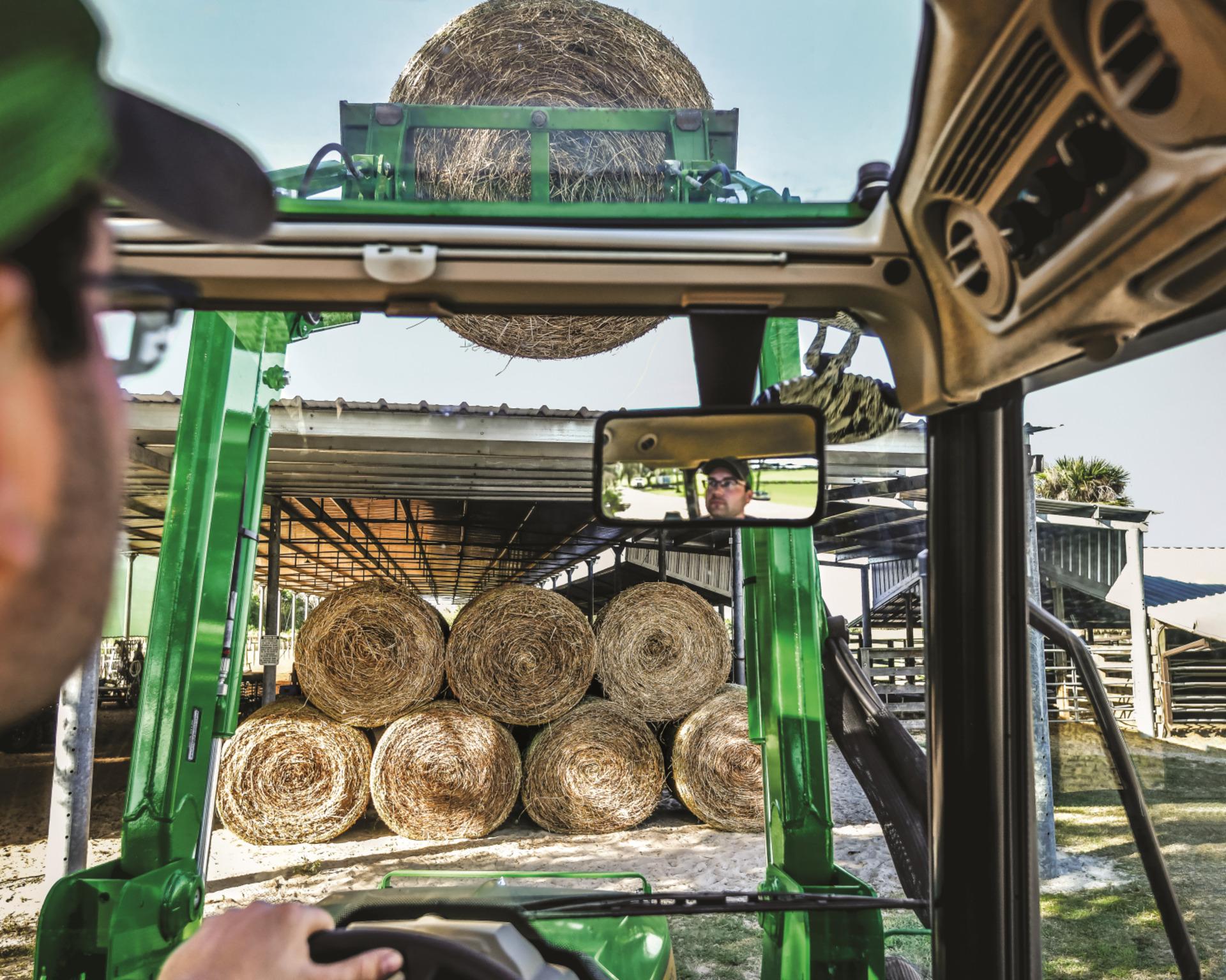 A first person view of a John Deere 5075E tractor working with hay bales.