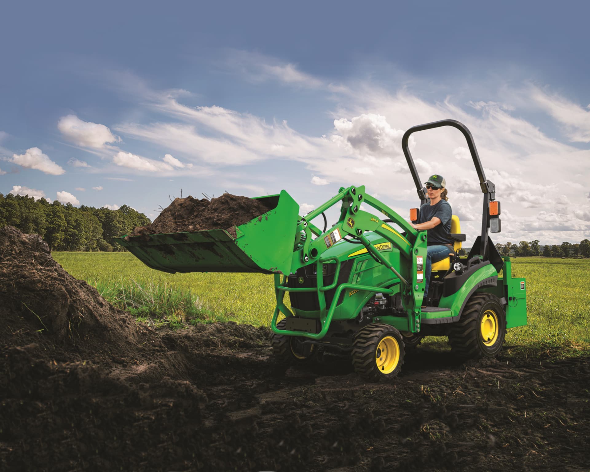 A homeowner moves soil with a front end loader on a John Deere tractor.
