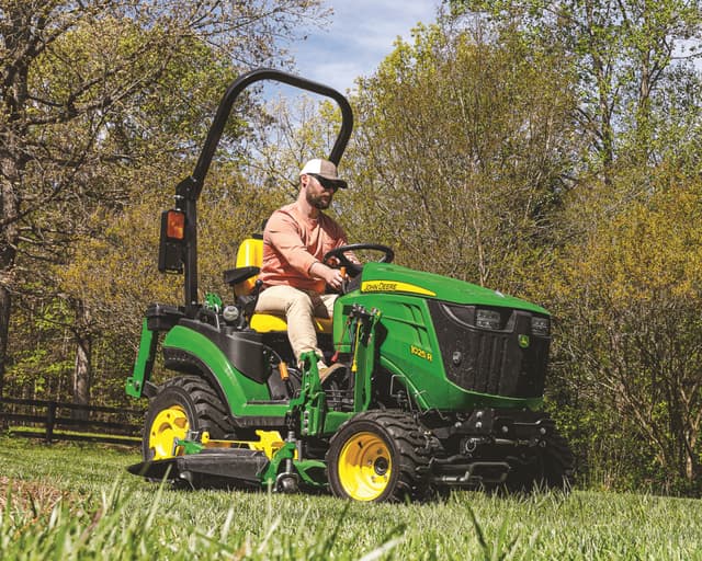 A John Deere compact tractor with a mower deck attachment for clearing grass and brush.