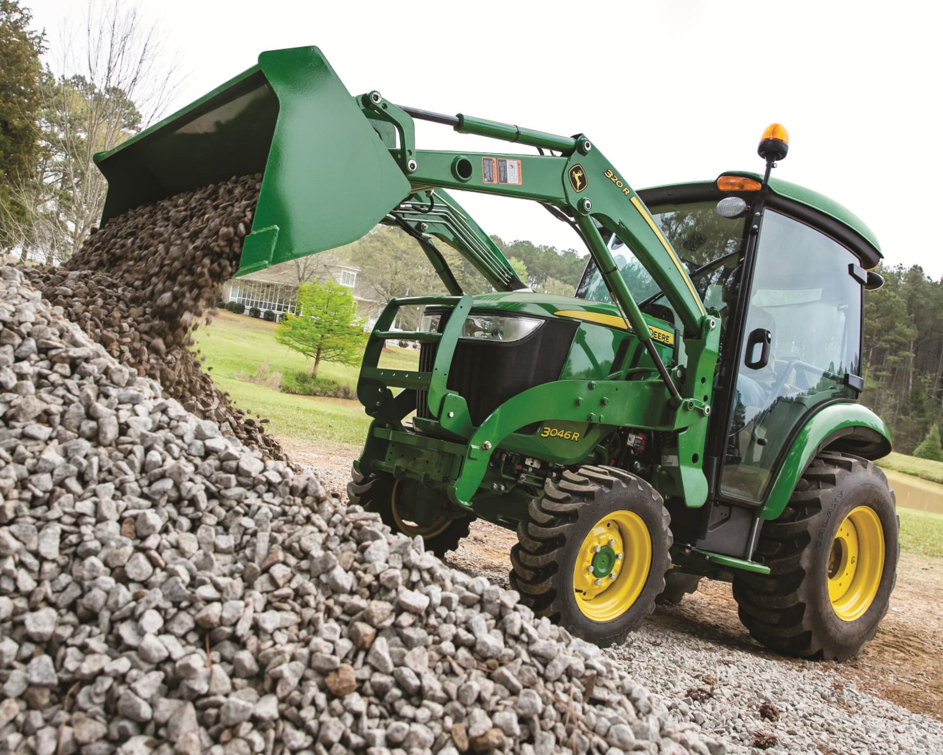 A John Deere tractor with a front-end loader attachment dumps gravel.