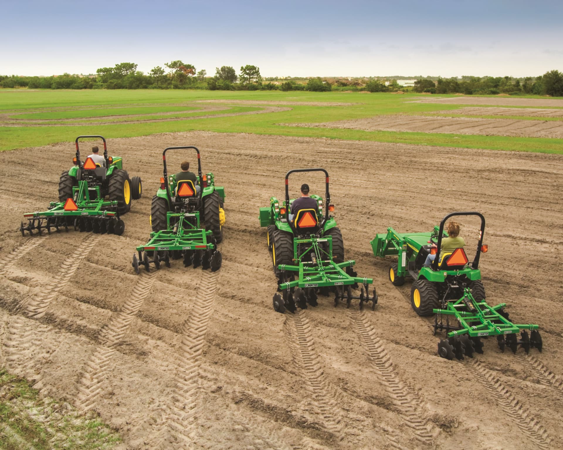 Four tractors with disc harrow attachments till a field.