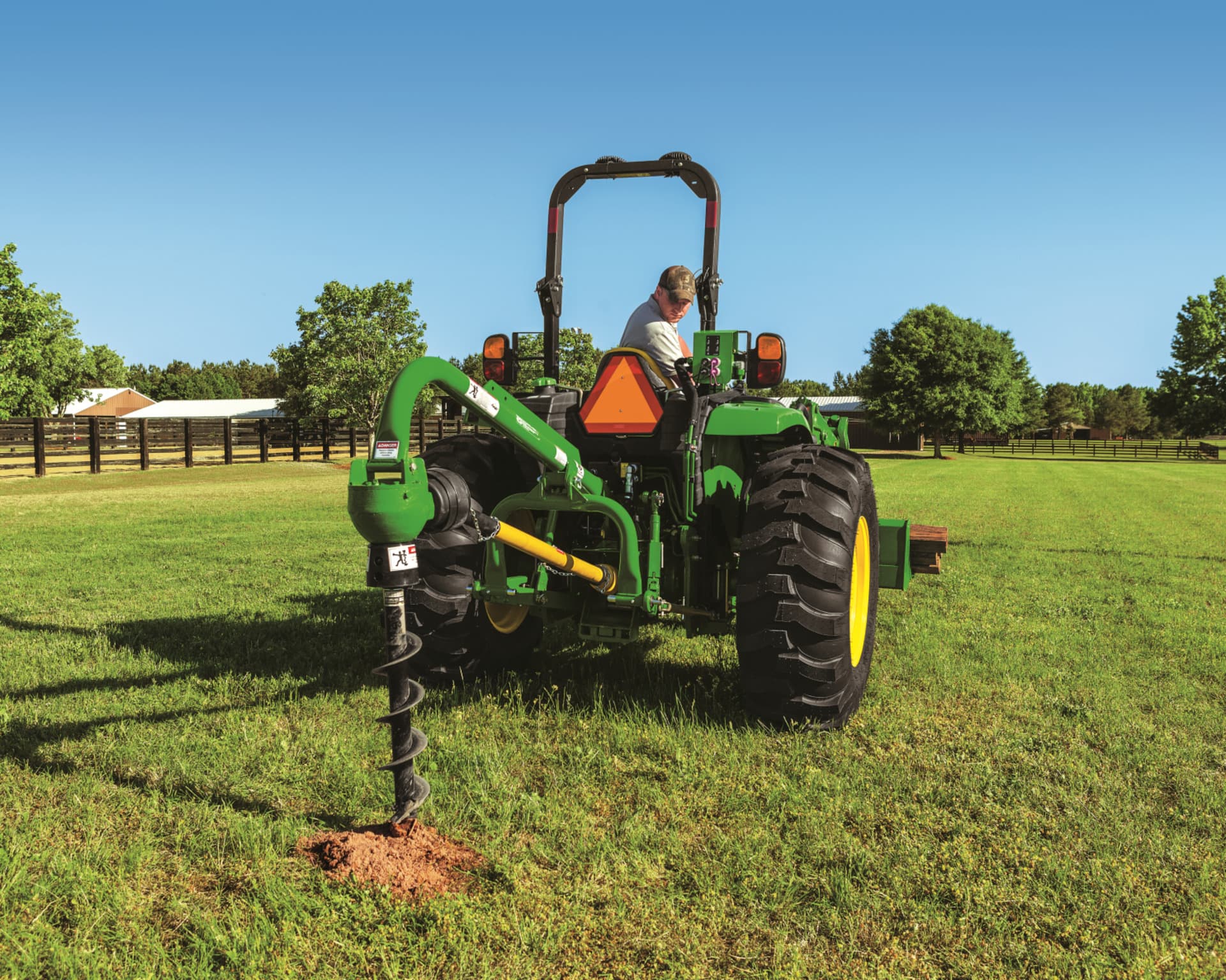 A tractor with a post hill digger attachments digs a post hole.