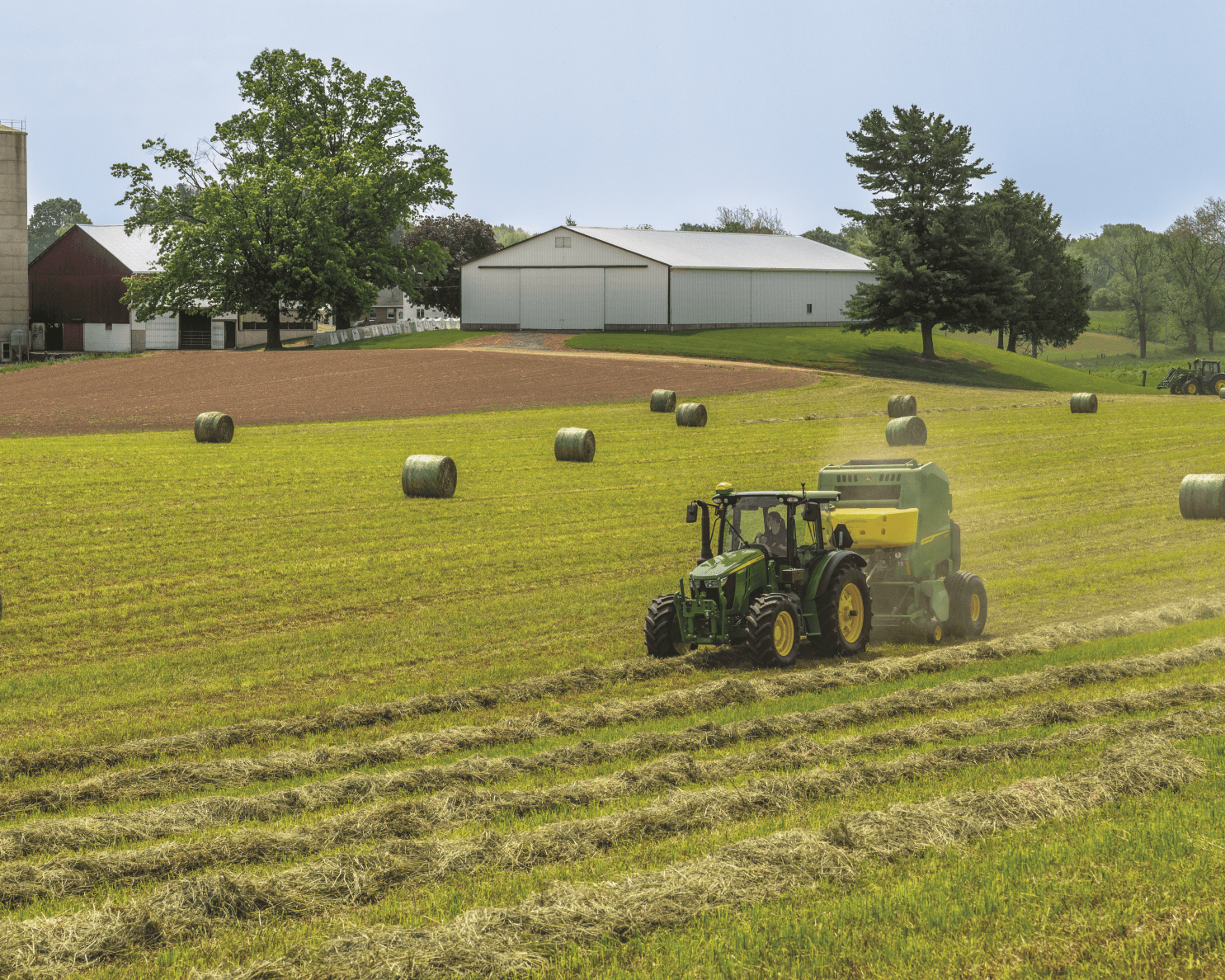 A John Deere tractor with a baling attachment bales hay in a field in Tennessee.