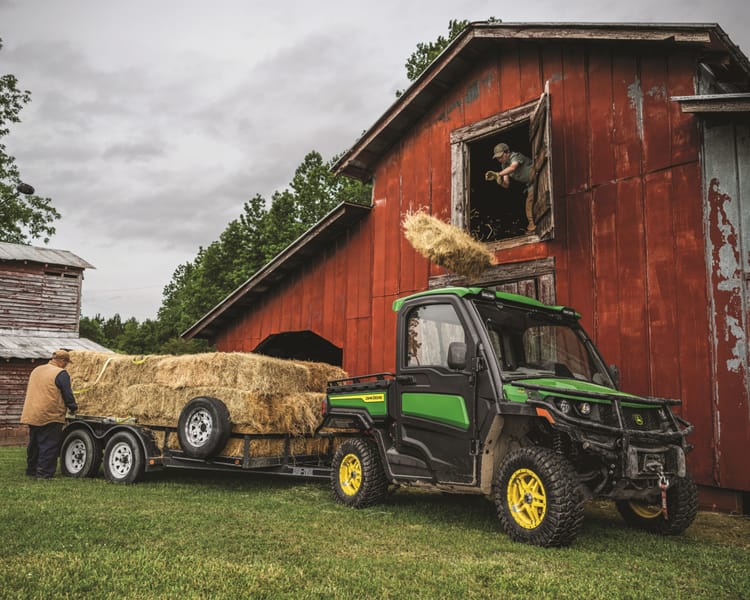 A Gator pulls a trailer with hay bales.
