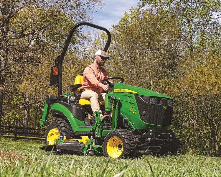 A John Deere compact tractor with a mower deck attachment for clearing grass and brush.