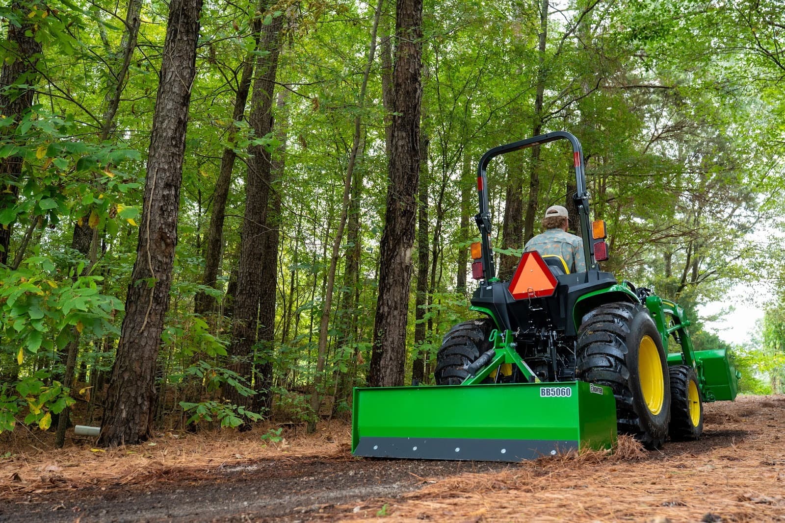 A property owner uses a John Deere 3 Series tractor with a box blade attachment to level land.
