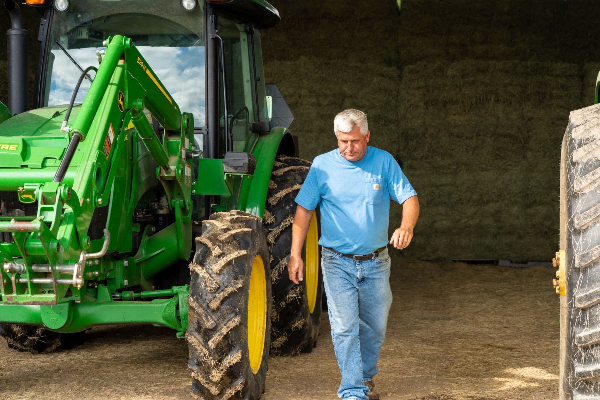 A farmer walks the property next to a John Deere enclosed cab tractor.